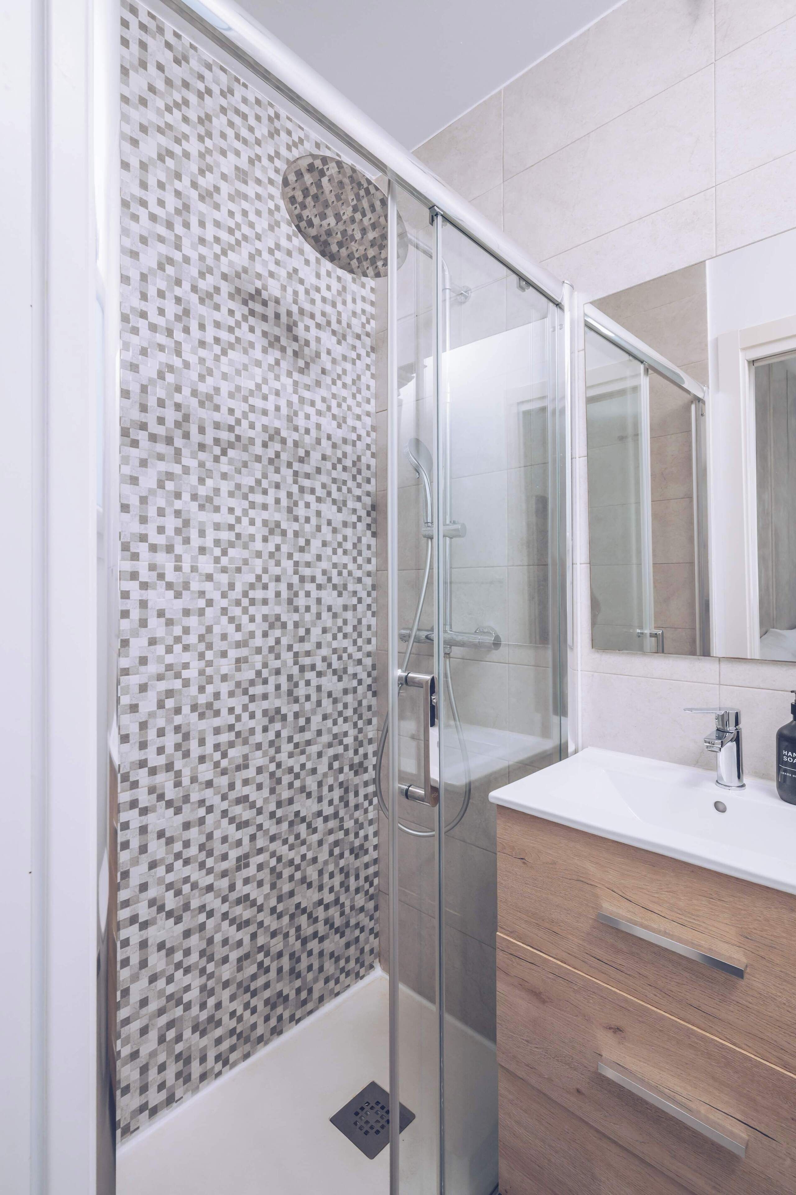 A modern bathroom with a glass shower enclosure, a white sink, and a wooden vanity.