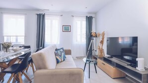 A modern living room with a sofa, dining table, chairs, a TV, and a lamp.