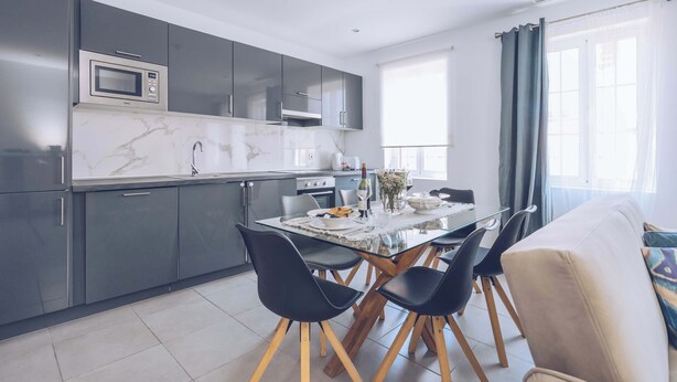 A modern kitchen with grey cabinets, a microwave, and a dining table with chairs.