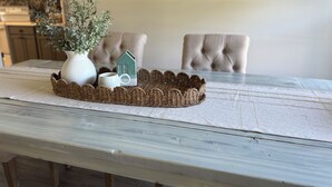 A dining table with a woven placemat, a white vase with green foliage, a ceramic house-shaped mug, and a white mug. - Beach Cottage: Cozy I Clean I Family I Beaches (Port St. Lucie)