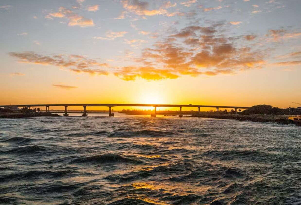 A sunset over a body of water with a bridge in the distance.