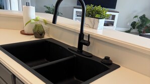 A kitchen with a double sink, dark cabinets, and a white countertop. - Beach Cottage: Cozy I Clean I Family I Beaches (Port St. Lucie)
