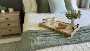A neatly made bed with a tray of items, a bedside table with a lamp, and a view of the outdoors. - Beach Cottage: Cozy I Clean I Family I Beaches (Port St. Lucie)