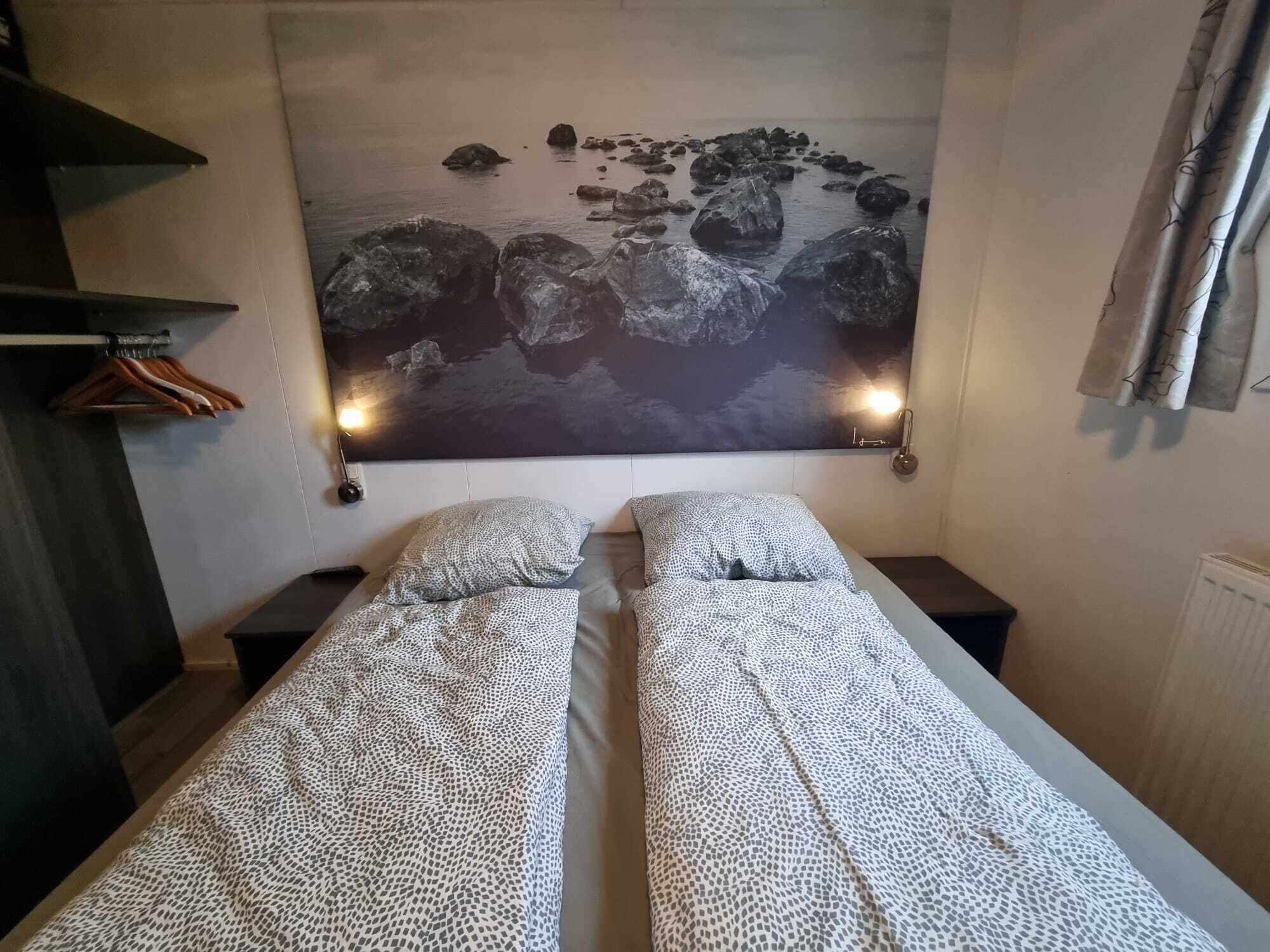 Une chambre avec deux lits, un grand tableau représentant des rochers et un radiateur.