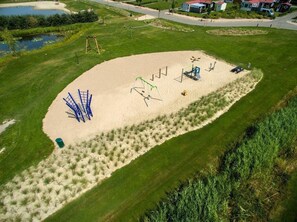 Eine Vogelperspektive eines Parks mit einem Sandspielplatz, Spazierwegen und einem Teich.