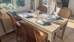 Een eetruimte met een houten tafel gedekt voor vier personen, rieten stoelen en uitzicht op het landschap door grote ramen.