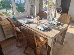 Ein Essbereich mit Holztisch, gedeckt für vier Personen, Korbstühlen und Blick ins Freie durch große Fenster.