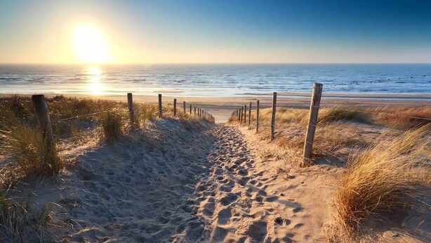 Een zandpad langs het strand, met een houten omheining die naar de oceaan leidt.