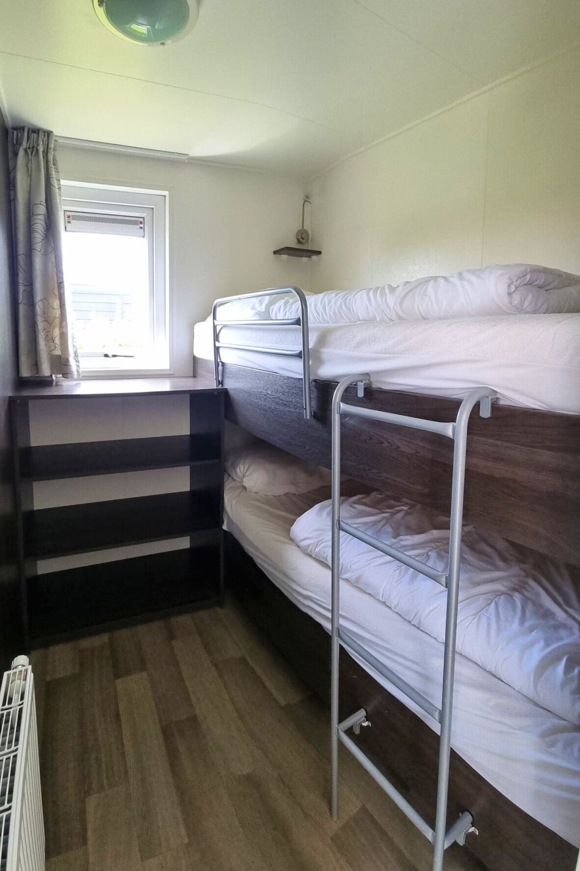 A bunk bed room with a window, a radiator, and a small shelf.