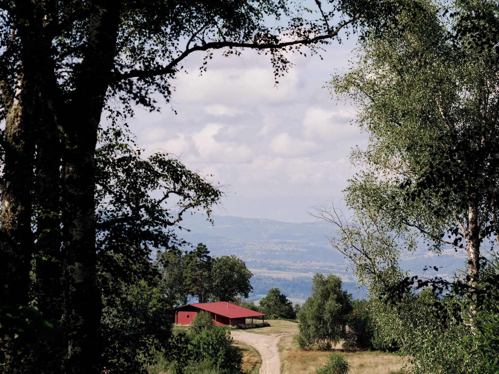 A rural landscape with a red building, surrounded by trees and a clear sky.