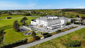 A large white building with multiple wings, surrounded by green fields and a clear sky.