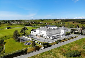 A large white building with multiple wings, surrounded by green fields and a clear sky.