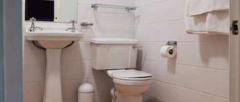 Une salle de bain avec un lavabo sur colonne, des toilettes et une étagère en verre.