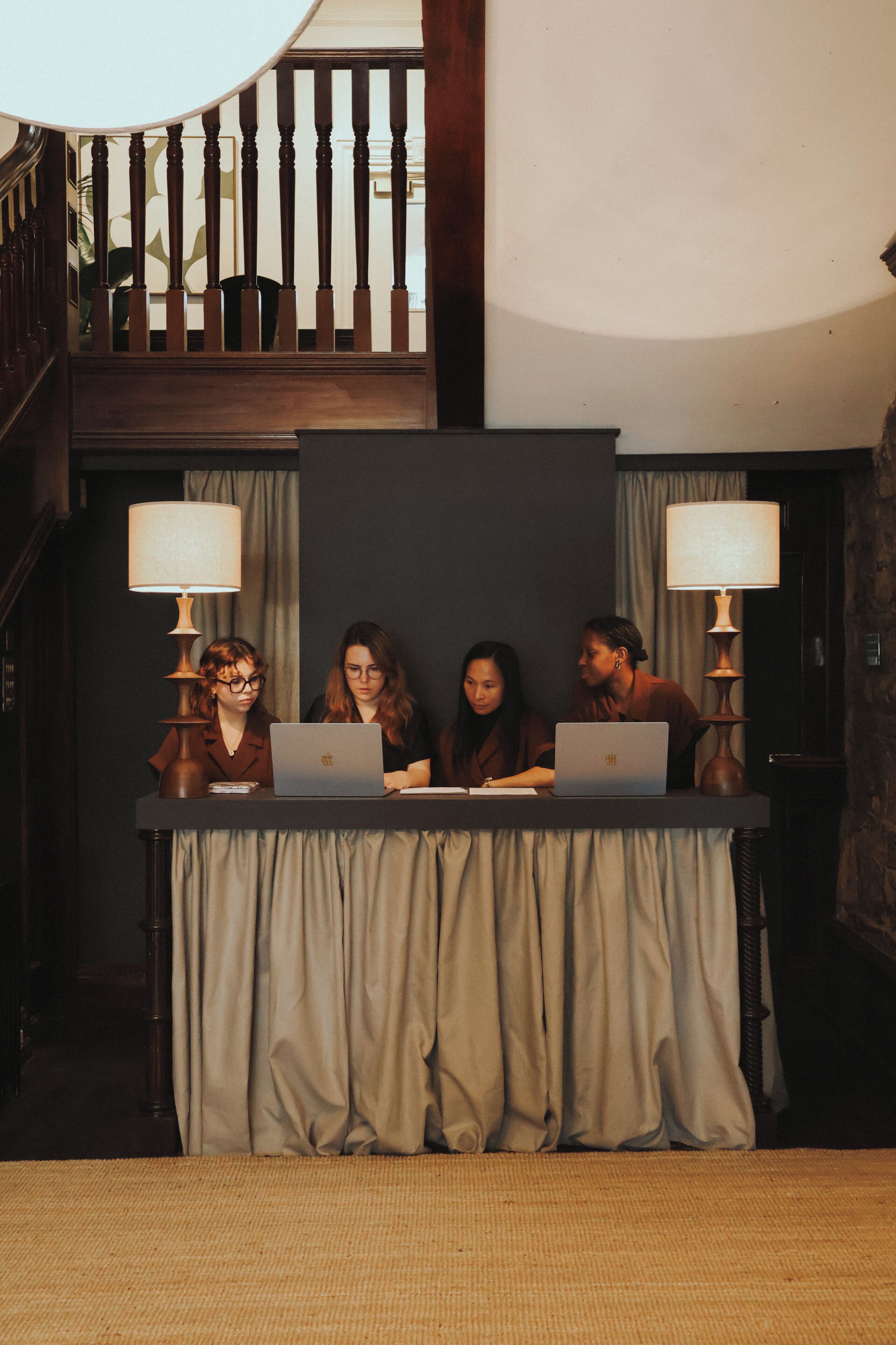 A room with a staircase, a table with a laptop, and two lamps.