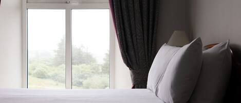 A hotel room with a bed, a lamp, and a window with curtains.