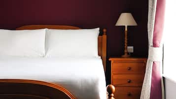 A bed with white bedding, a wooden headboard, a nightstand with a lamp, and a patterned curtain.