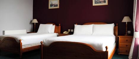 Two wooden beds with white linens, a nightstand with a lamp, and two framed pictures on the wall.
