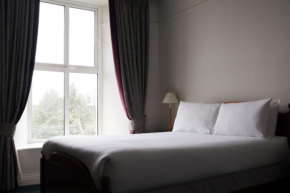Une chambre dâhĂŽtel avec un lit, des rideaux, une lampe et une fenĂȘtre.