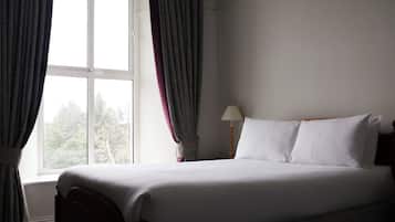A hotel room with a bed, curtains, a lamp, and a window.