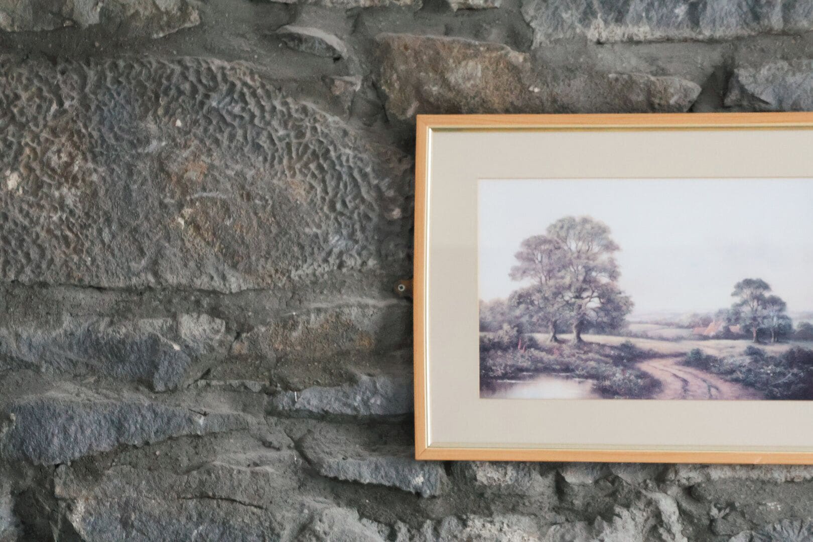 A framed landscape painting on a stone wall.