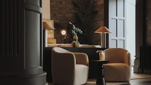 A modern living room with a sofa, two armchairs, a side table, a floor lamp, and a potted plant.