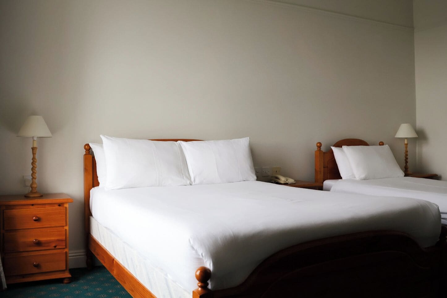 Habitación de hotel con dos camas individuales, cabeceros de madera, mesitas de noche con lámparas y un pequeño aparador.