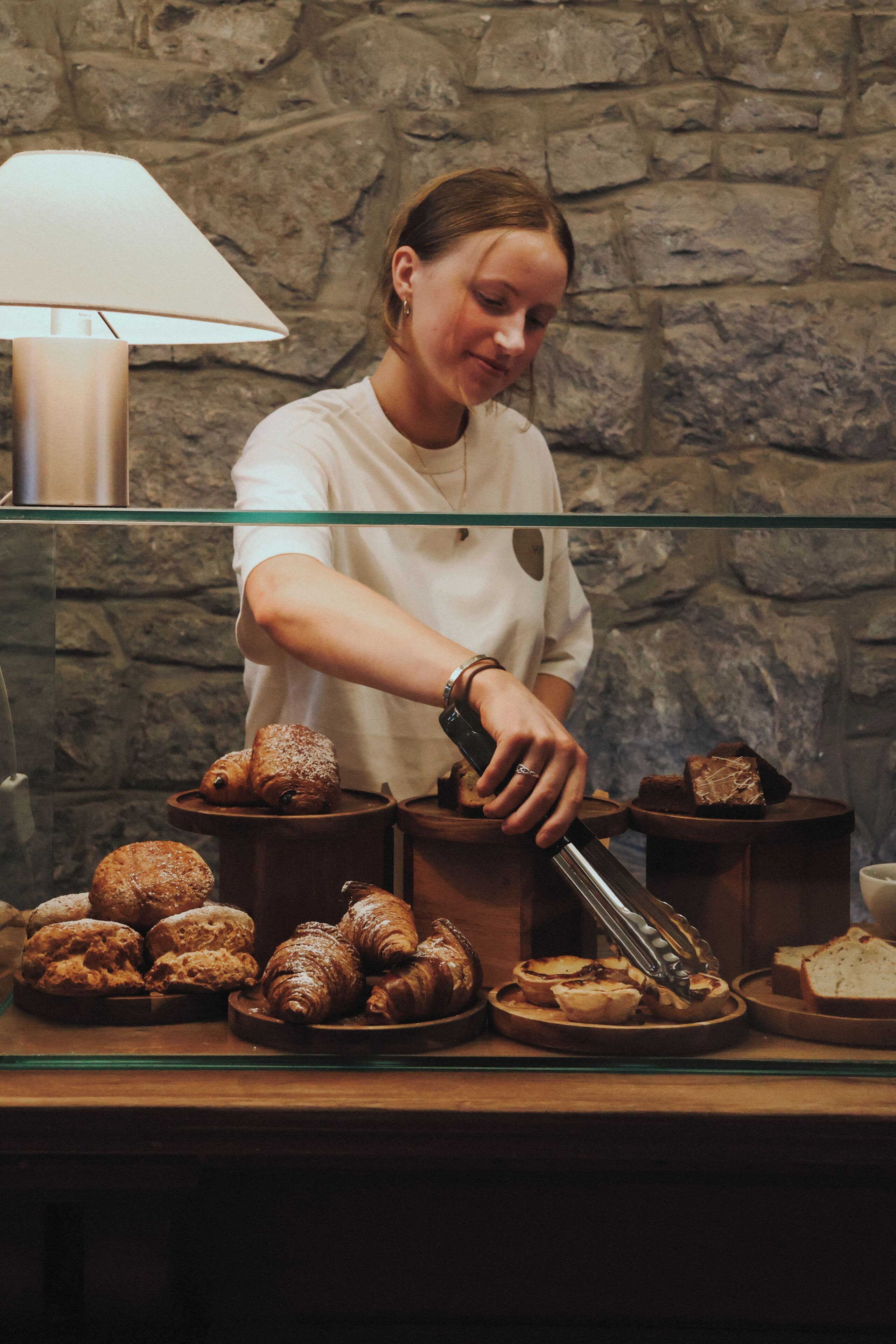 A person arranging pastries on a counter with a stone wall background.