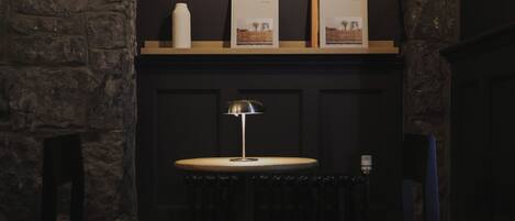 Una habitación oscura con una mesa redonda, una lámpara y cuadros en estantes.