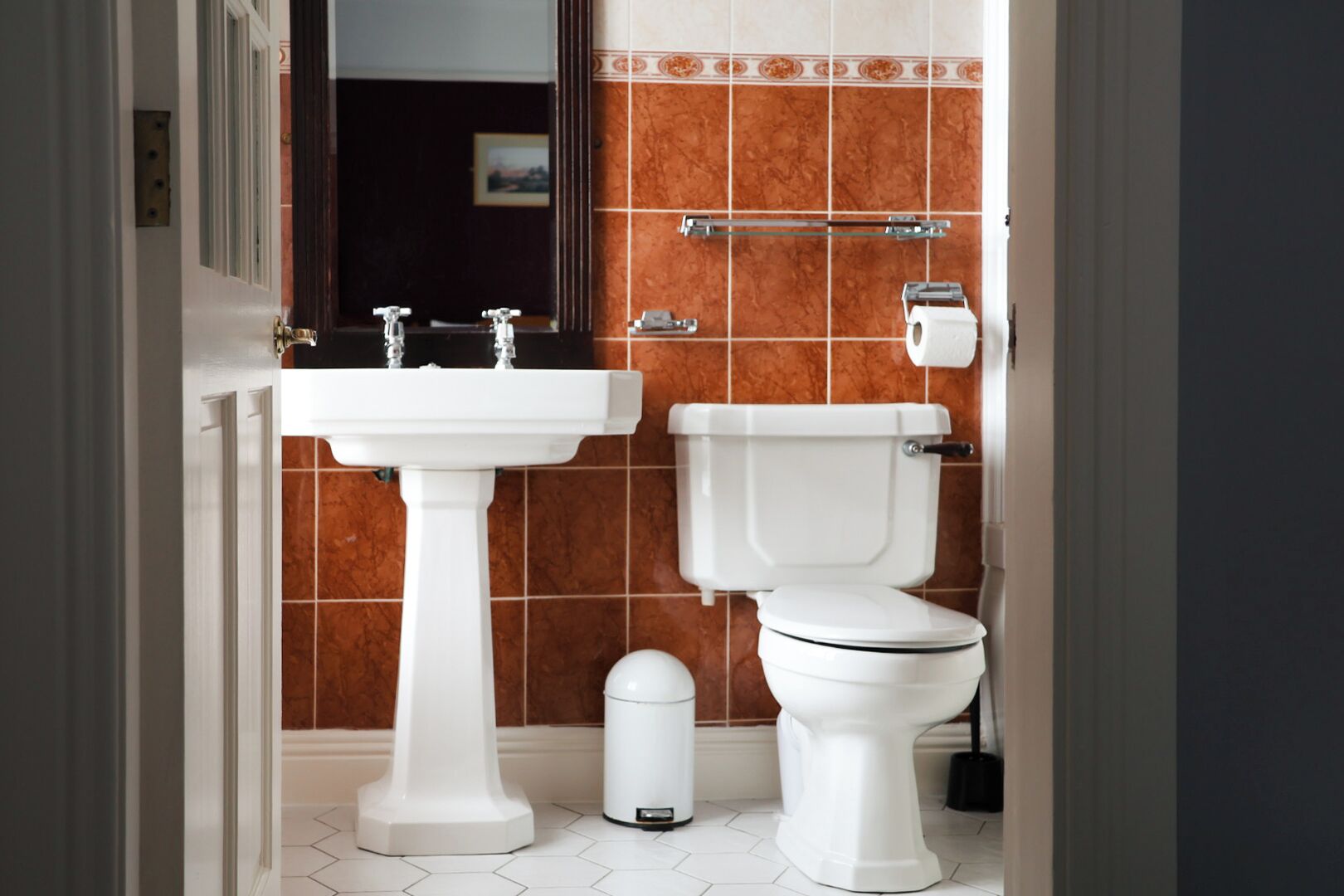 Un baño con lavamanos pedestal, inodoro y cubo de basura.