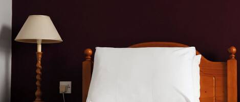 Una cama con ropa de cama blanca, un cabecero de madera, una lámpara de noche y un cuadro en la pared.