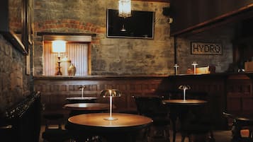 Zona de bar tenuemente iluminada, con paredes de piedra, muebles de madera y un televisor en la pared.