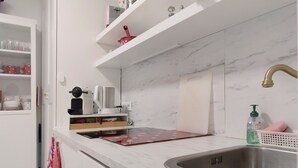 Une cuisine dotée d’un plan de travail en marbre, d’un évier en acier inoxydable et d’une casserole rouge posée sur l’étagère.