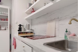 A kitchen with a marble countertop, a stainless steel sink, and a red pot on the shelf.