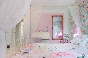 A bedroom with a bed, a vanity with a mirror, and a door leading to another room.