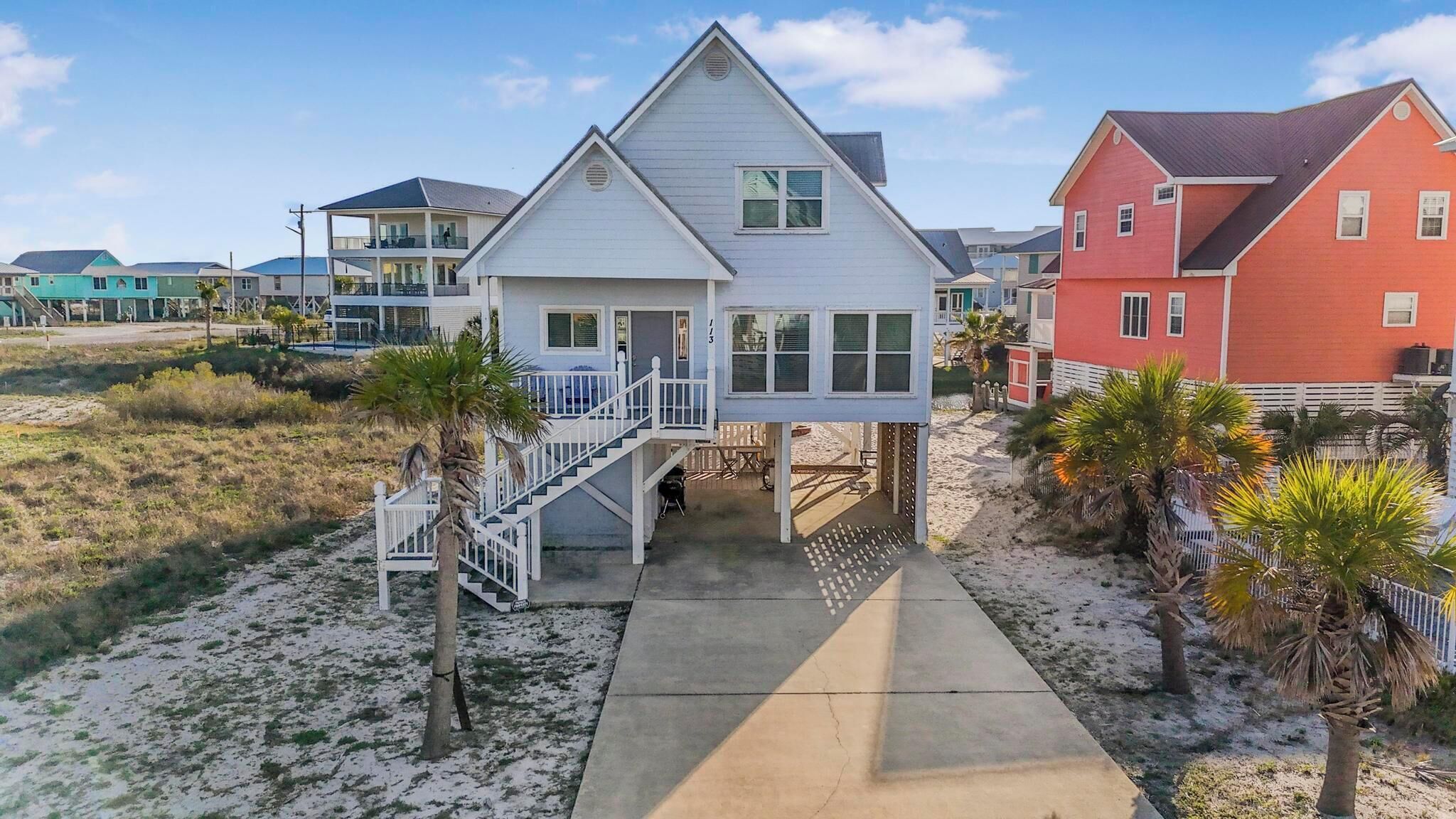 Ein Strandhaus mit überdachter Veranda, einer Treppe und einem Kiesweg.