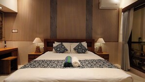 A hotel room with a large bed, two bedside tables with lamps, a wooden headboard, and a view through a glass door. - Danu House Ubud (Ubud)