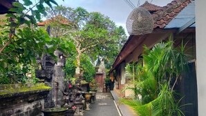 A narrow pathway flanked by traditional buildings, with stone statues and potted plants. - Danu House Ubud (Ubud)