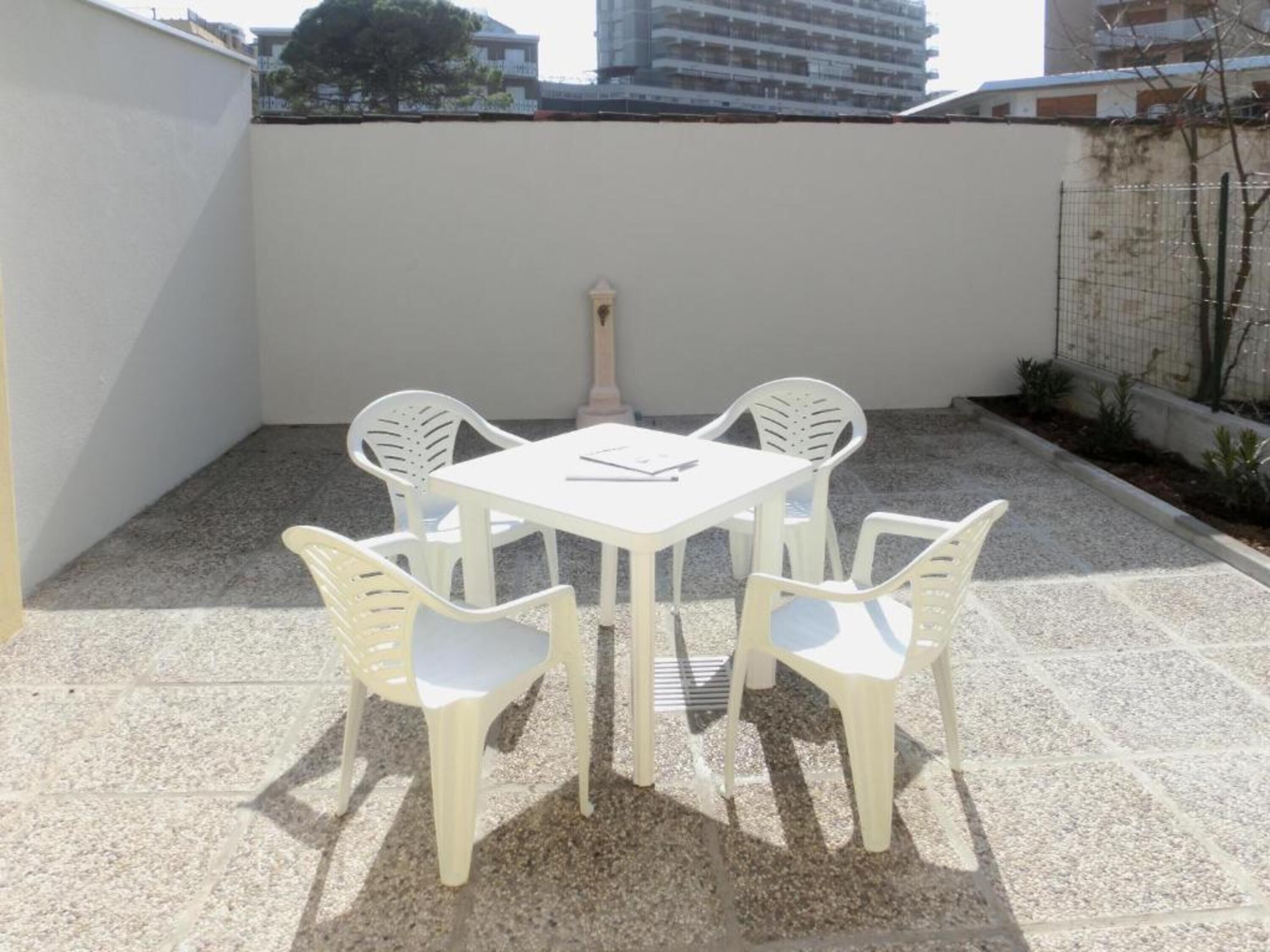 Un patio con una mesa blanca y cuatro sillas blancas, rodeado por un muro blanco bajo y un suelo de grava.