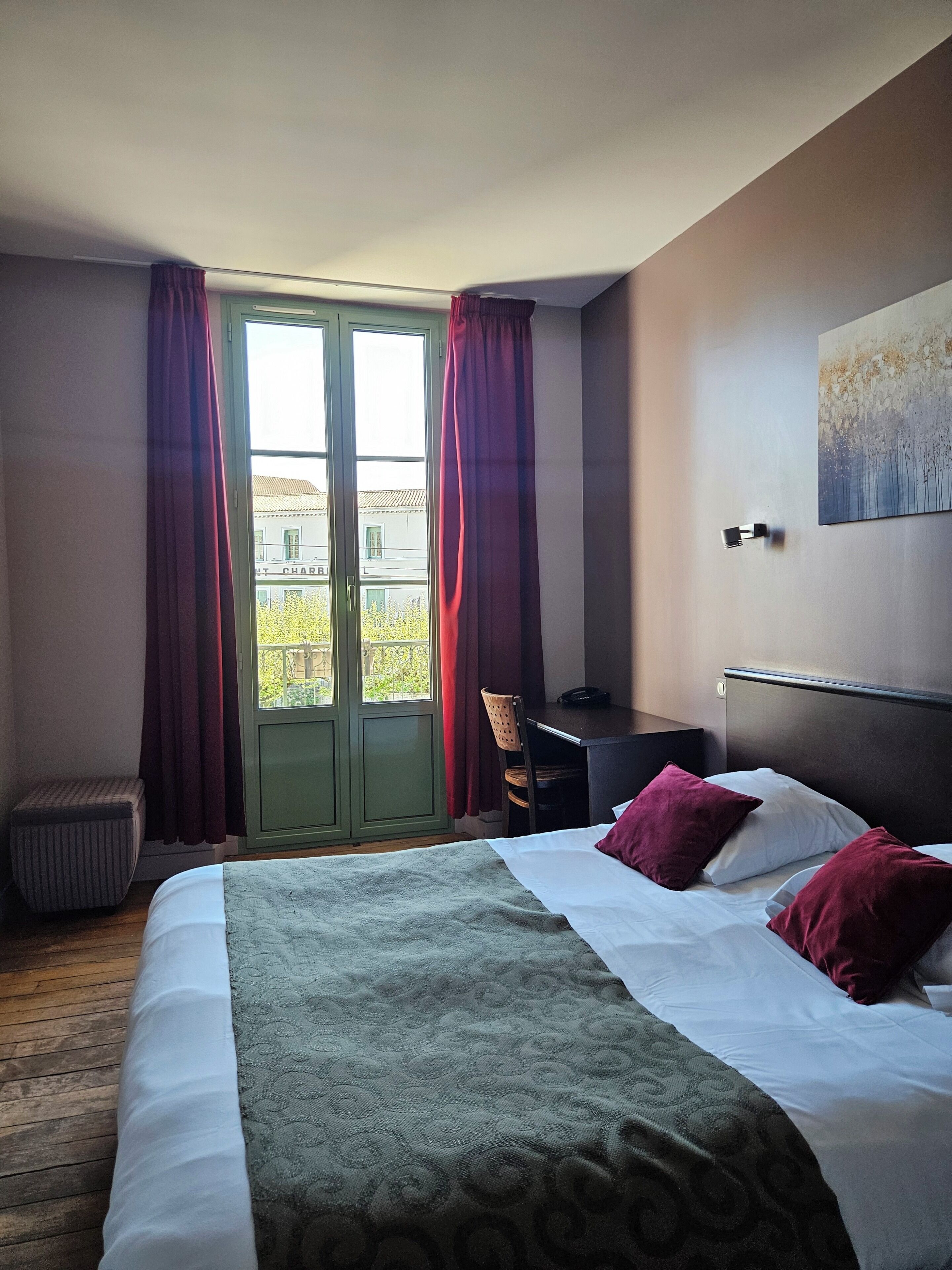 Habitación de hotel con cama, escritorio, silla, ventana con cortinas y un cuadro en la pared.