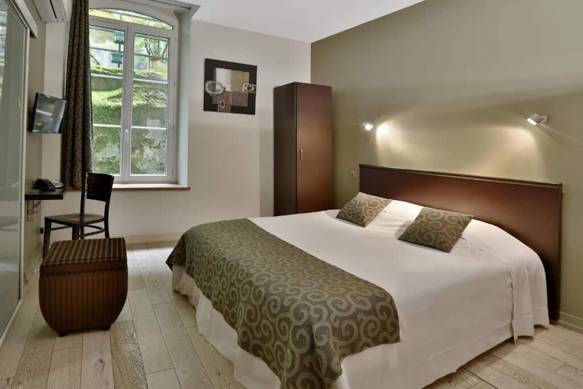 Un dormitorio con cama, una silla, un armario, un escritorio y una ventana.