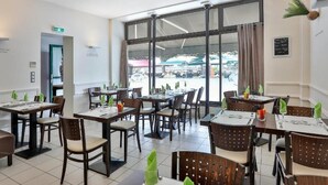 Un restaurante con varias mesas y sillas, ventanas amplias y vistas al exterior.