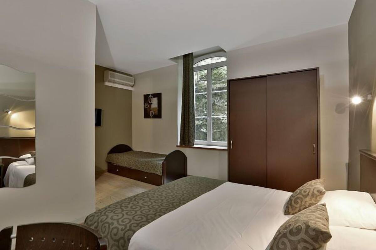 Un dormitorio con cama, una silla, armario, ventana y equipo de aire acondicionado.