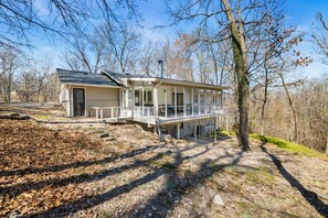 Ein zweigeschossiges Haus mit einer Veranda, einer Garage und einem bewaldeten Hintergrund.