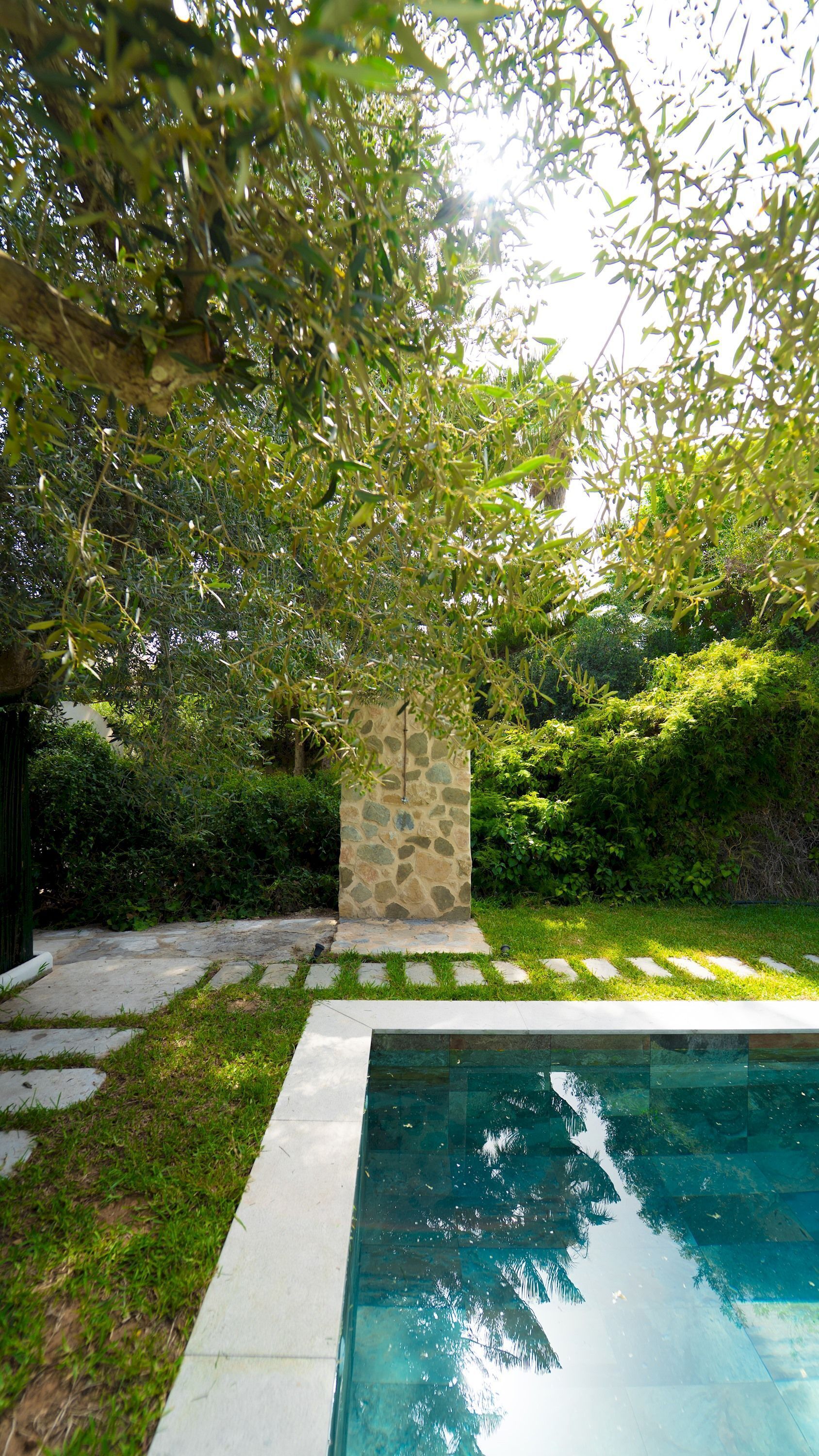 A swimming pool with a stone pillar and surrounding greenery.