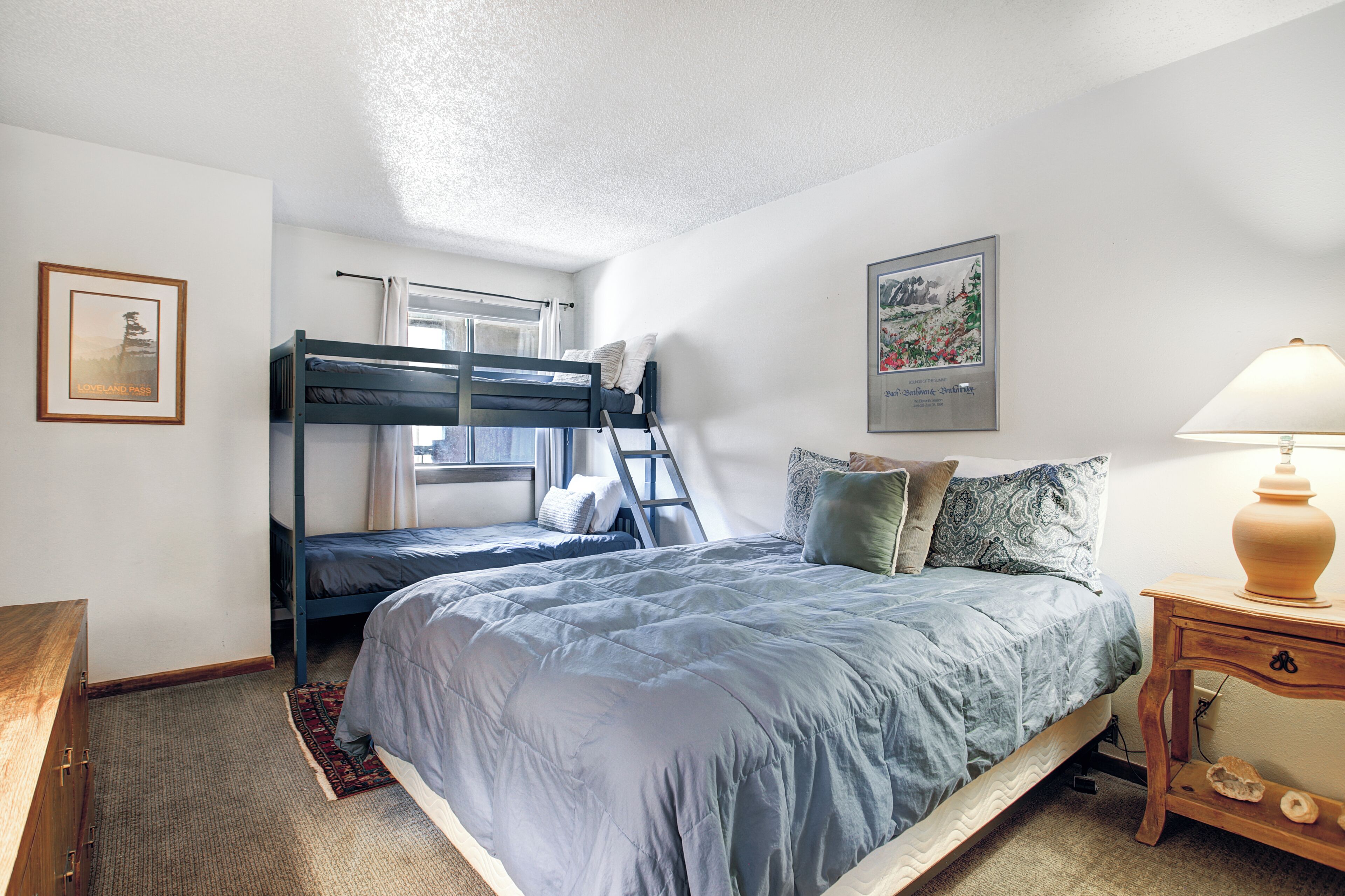 A bedroom with bunk beds, a desk, a lamp, and framed pictures on the walls.