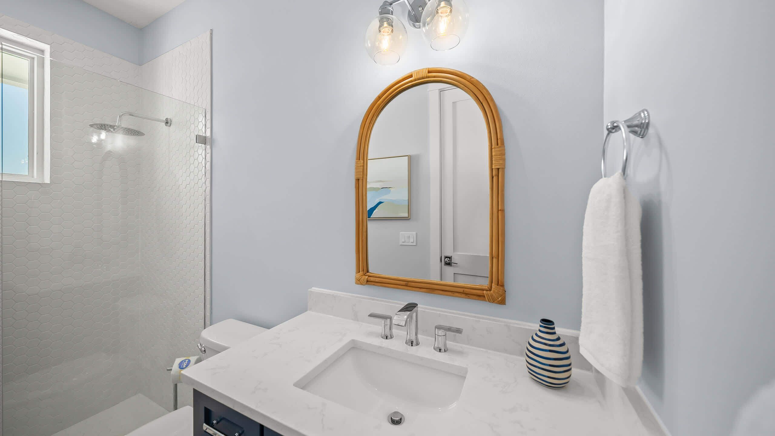 A bathroom with a shower, a sink, a mirror, and a vase.