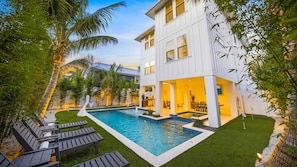 A modern two-story building with a swimming pool, outdoor seating, and lush greenery. - Heated Pool/Spa - Rooftop Deck - Walk to the Beach (Bradenton Beach)