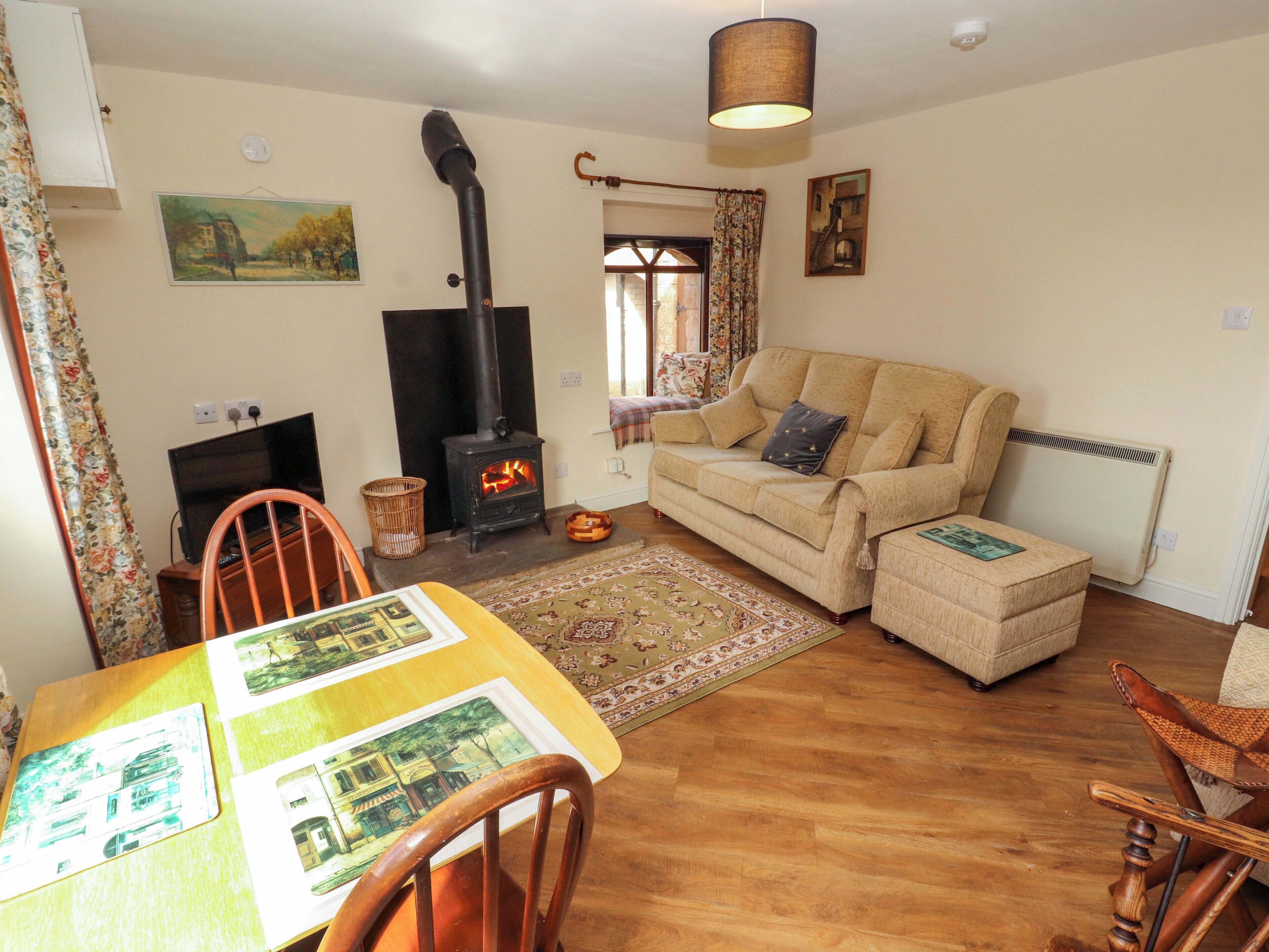 Una sala de estar acogedora con un sofá, una mesa con un mantel individual, una chimenea, una lámpara colgante y una ventana con cortinas.