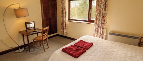 A bedroom with a bed, a desk with a computer, a chair, a lamp, and a window with curtains.