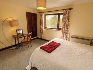 A bedroom with a bed, a desk with a computer, a chair, a lamp, and a window with curtains.